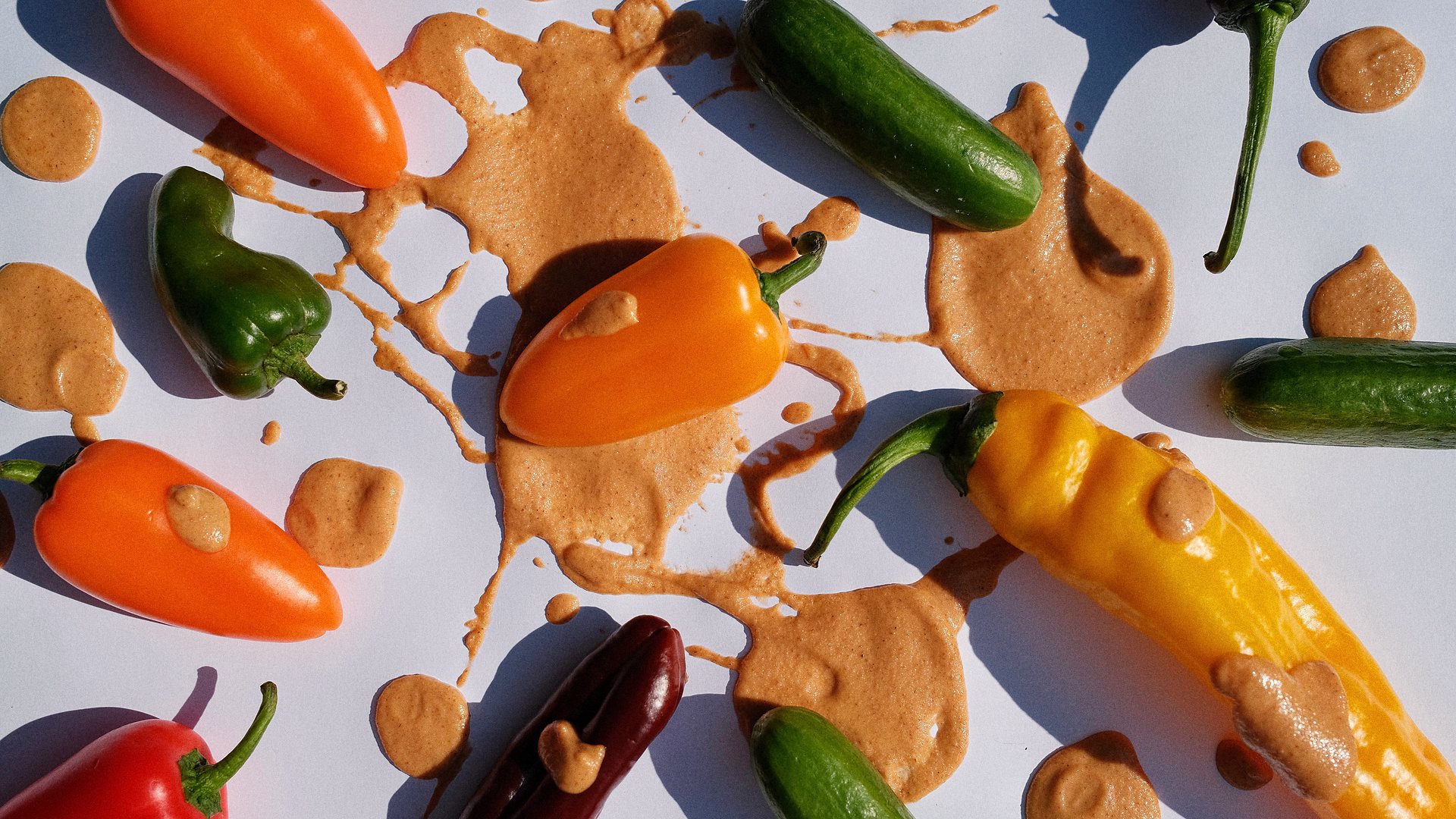 Oh Mommy! sauce splashed across a table scattered with peppers and cucumbers.