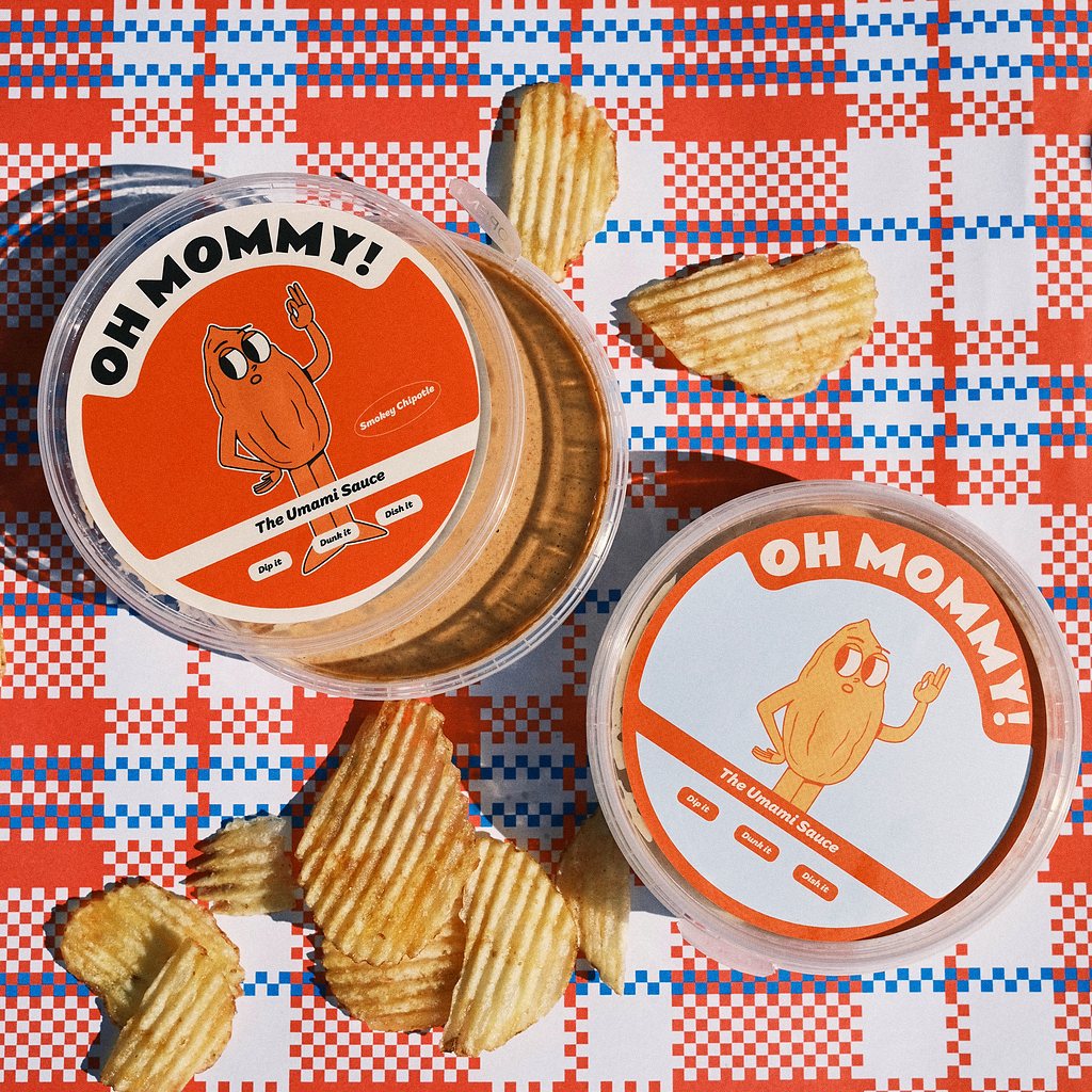 Two tubs of Oh Mommy! sauce on a red gingham cloth with crinkle-cut crisps.